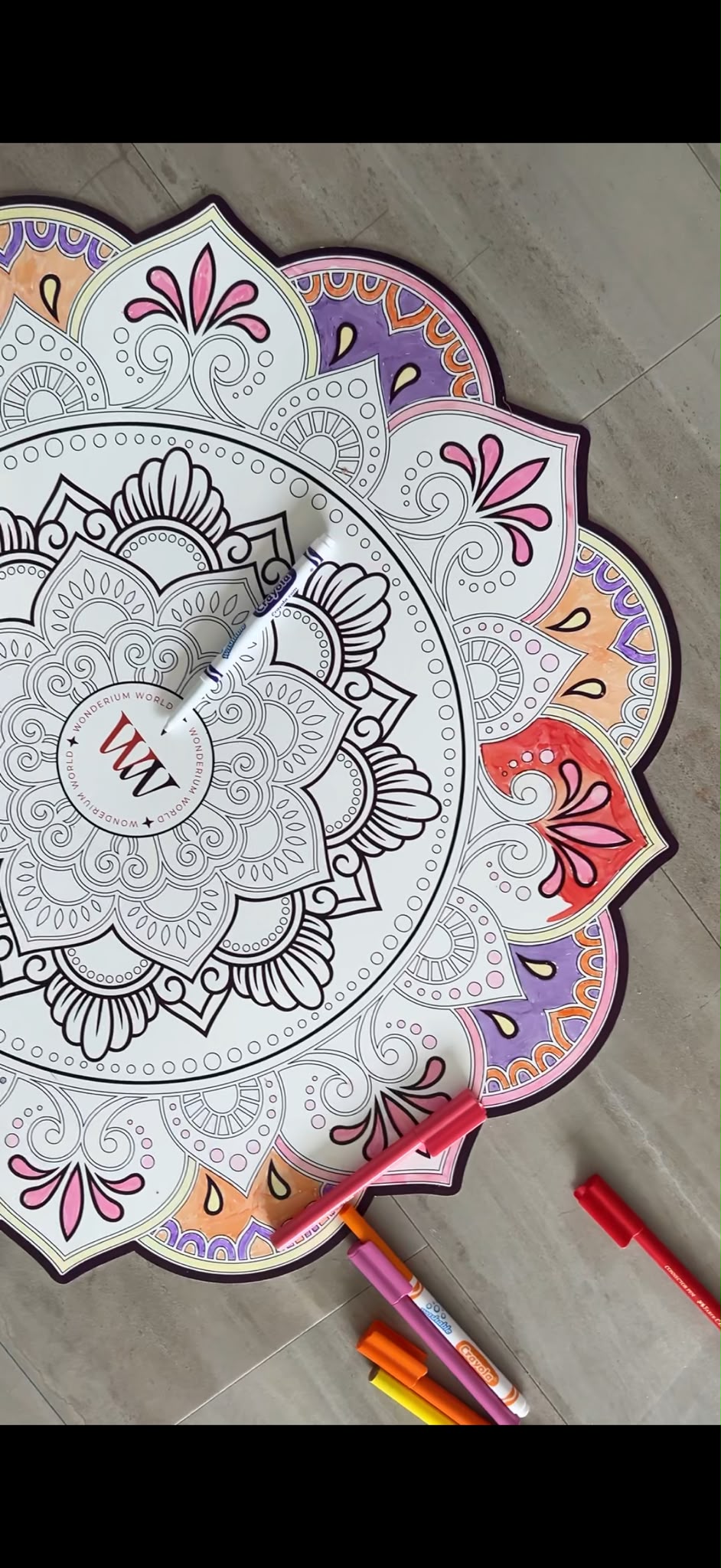 Wonderium Mindful Mandala mat, partially coloured in pink, purple, orange and yellow, with markers beside it.