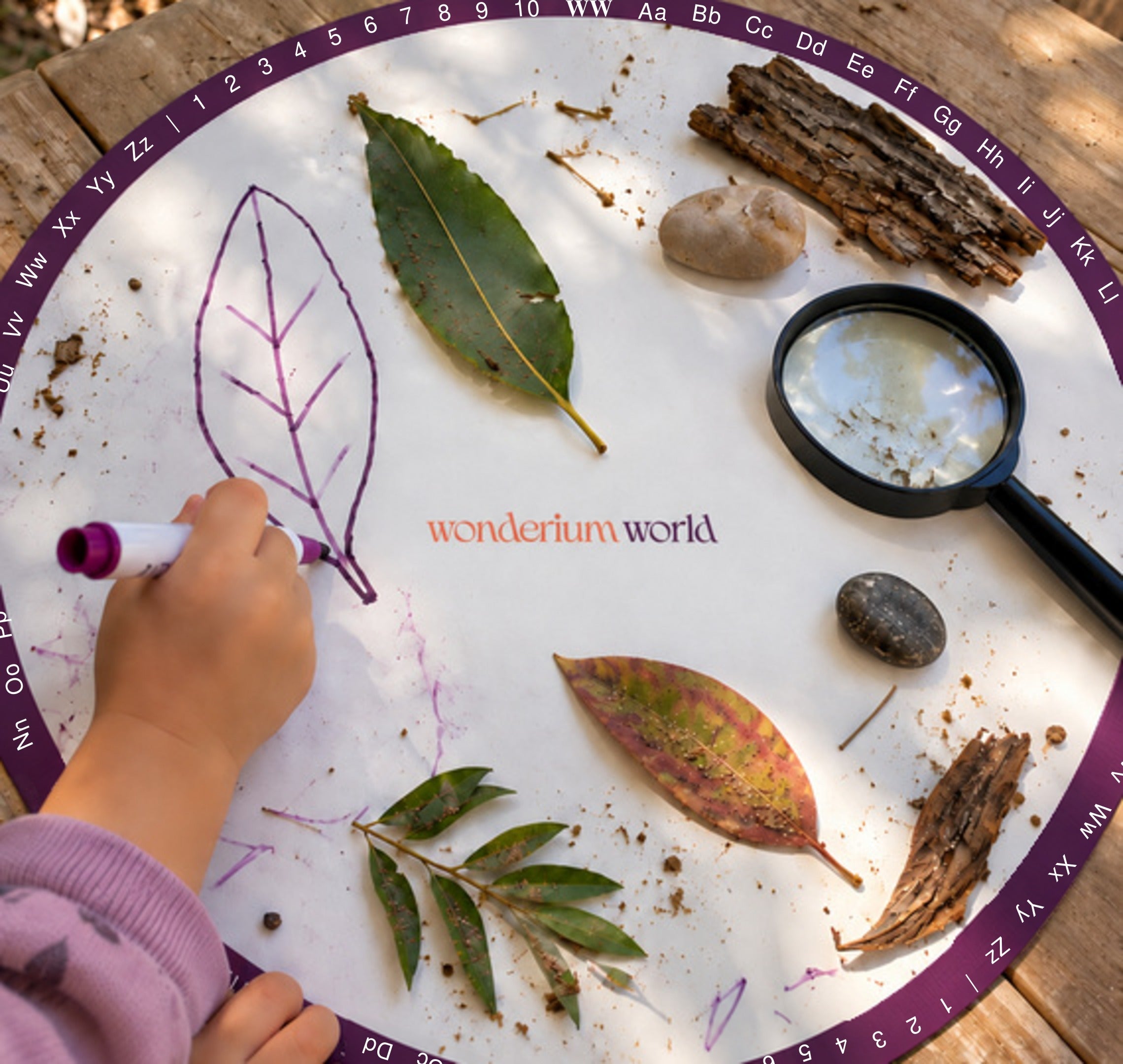 A child drawing a leaf beside leaves, bark, stones and a magnifying glass on a Wonderium learning mat