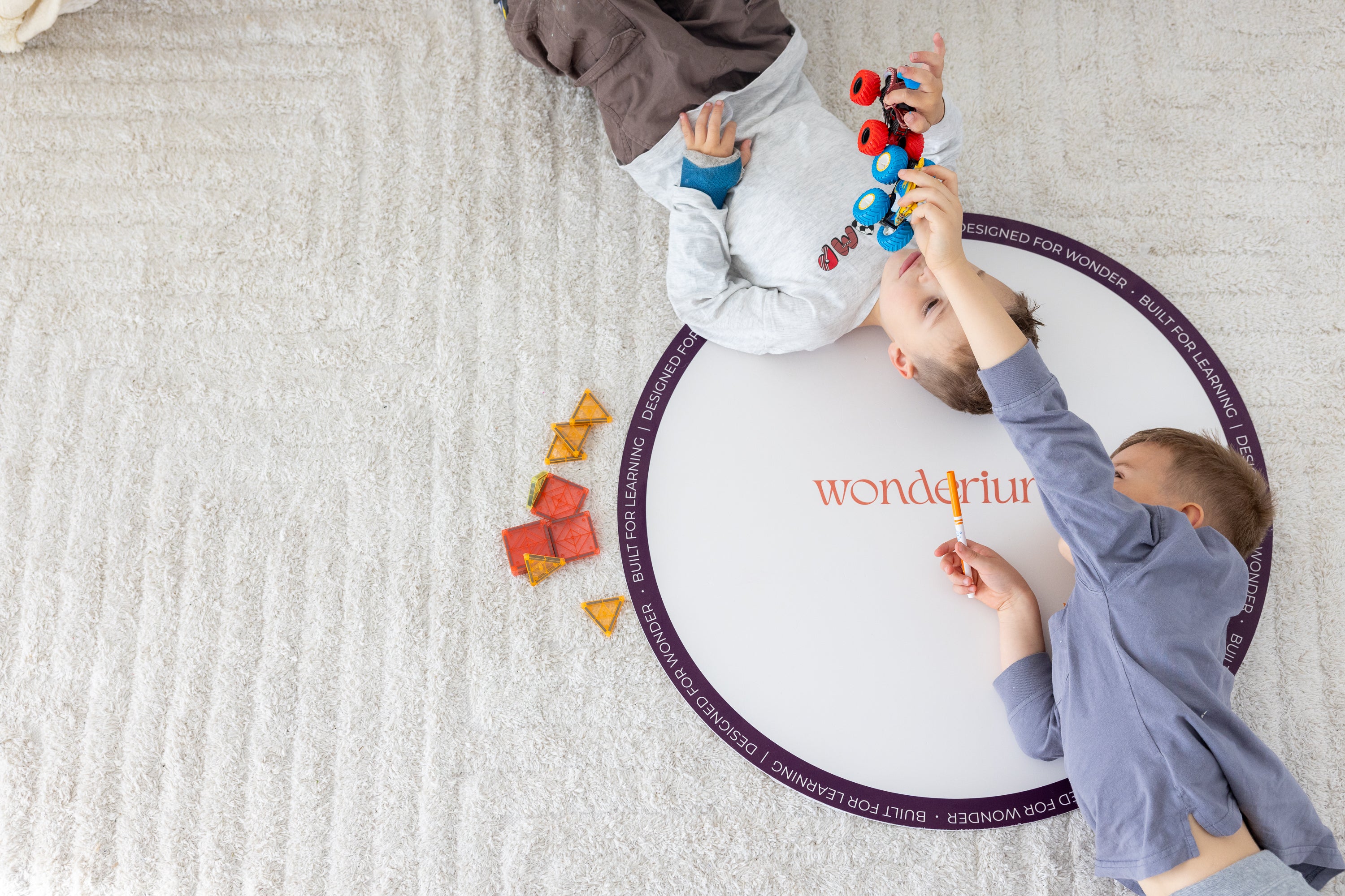 Two children sharing toy cars and creative play beside a Wonderium mat